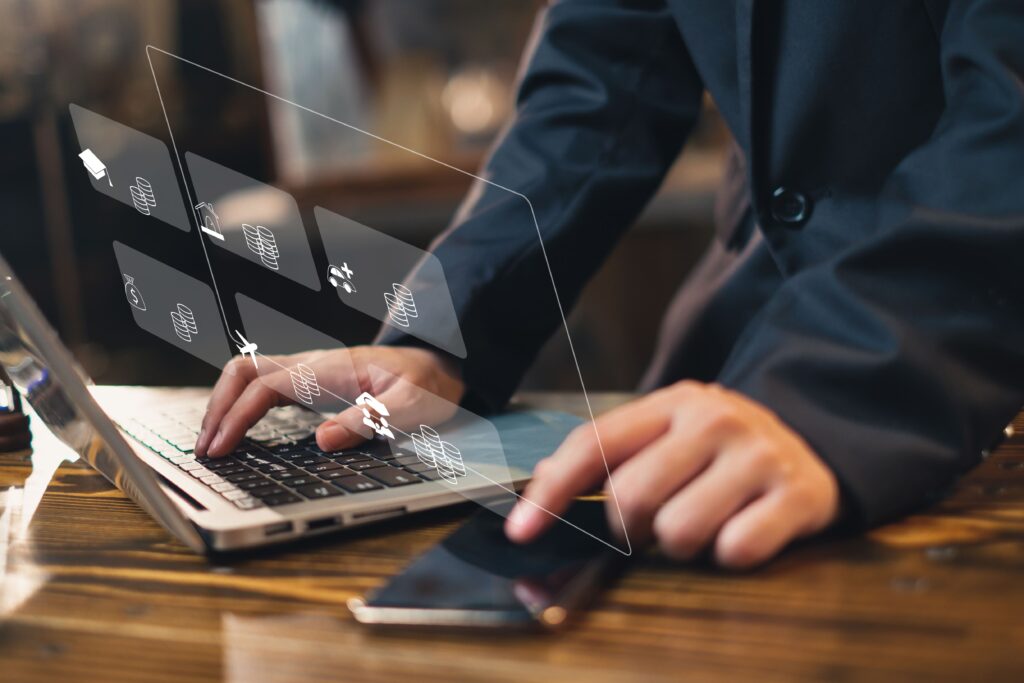 Eine Person tippt auf der Tastatur eines Laptops und im Vordergrund sind animierte Symbole zu dem Thema Finanzen zu erkennen