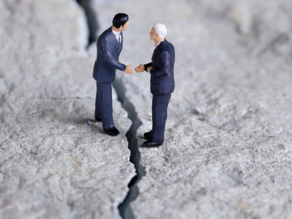 Zwei Figuren im Anzug reichen sich über einen Graben die Hand-symbolisch für Einigung bei komplexen Themen wie Betriebsaufspaltung.